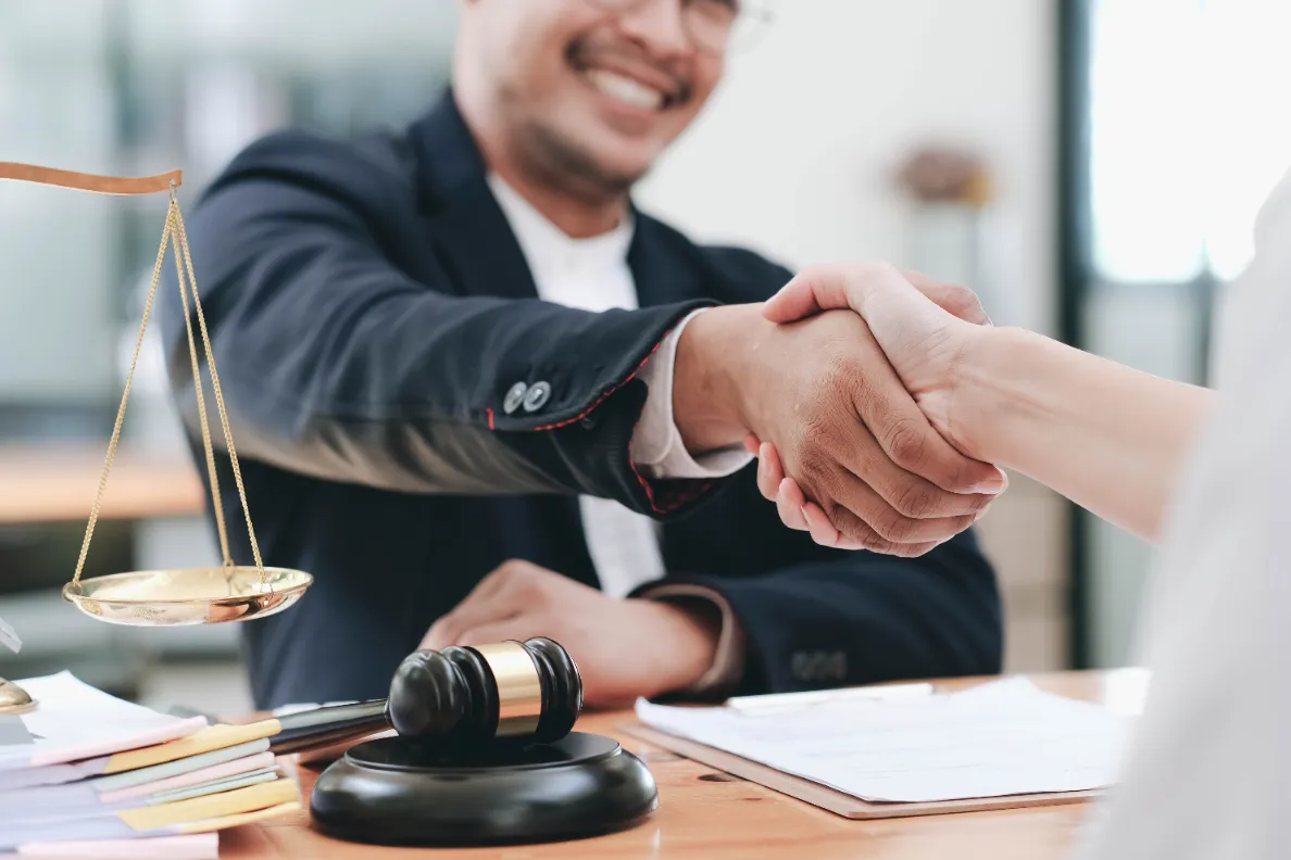 A bail bonds agent giving a handshake to a client with a gavel and a scale on the side.